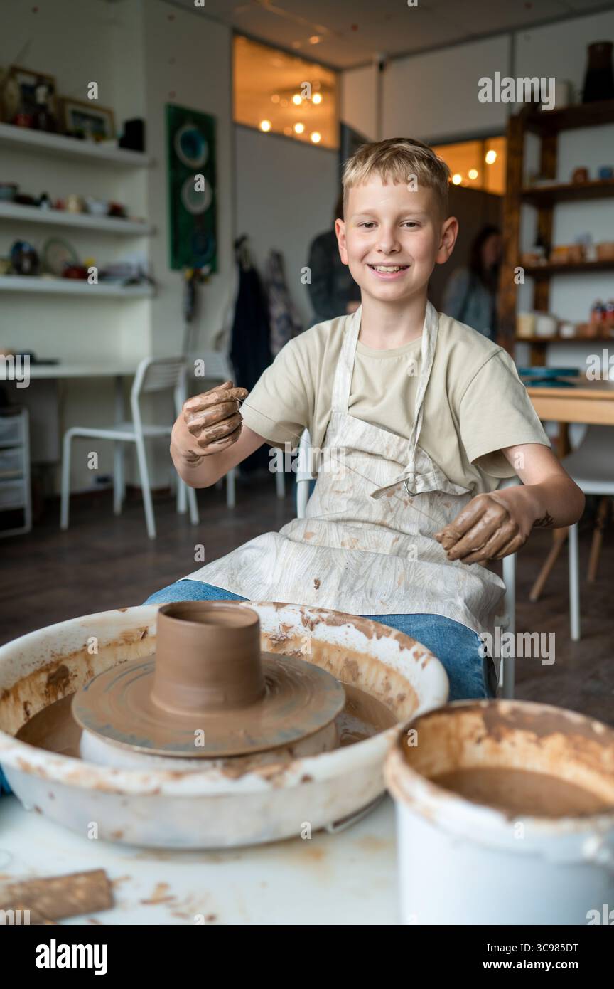 I ragazzi biondi imparano la ceramica, primo piano delle mani che modellano l'argilla su una ruota, attività creative per i bambini in un accogliente studio di ceramica, lavoro di squadra e abilità manuali Foto Stock