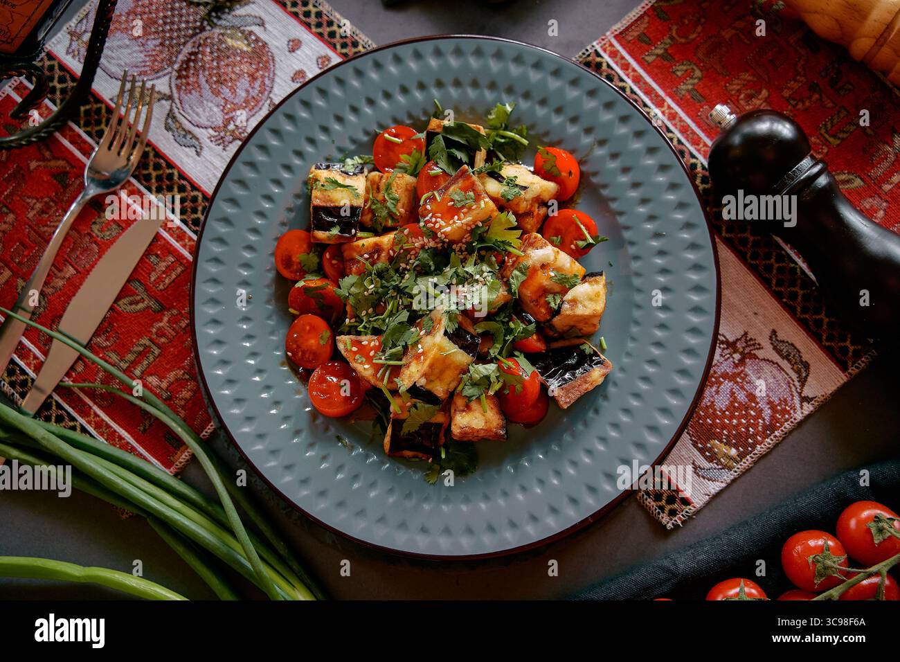 Piatto colorato con tofu alla griglia, pomodori ciliegini ed erbe fresche che esaltano la creatività culinaria e la nutrizione su un piatto strutturato Foto Stock