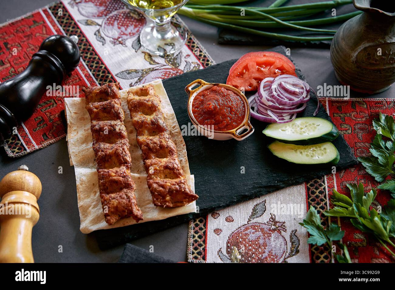 Un piatto di Kebab alla griglia servito con verdure fresche e salsa piccante su un tavolo rustico che mette in risalto la cucina culturale Foto Stock