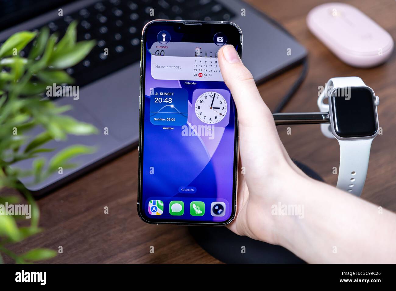 Poznan, Polonia - 29 luglio 2025: La mano di un utente interagisce con uno smartphone con ios 26 e Liquid Glass, visualizzando calendario, orologio e widget meteo Foto Stock