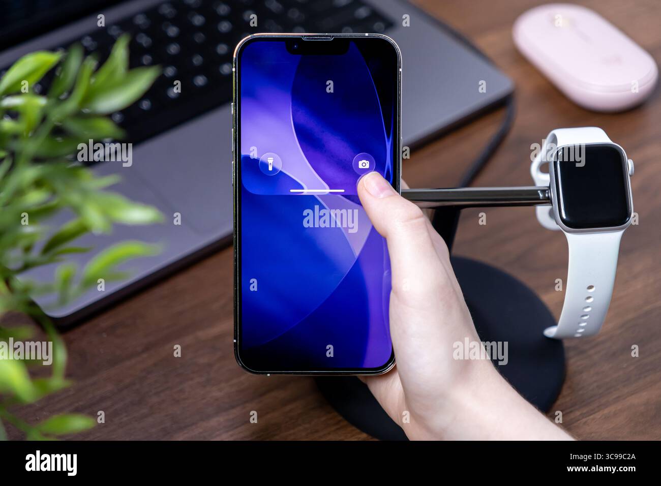 Poznan, Polonia - 29 luglio 2025: Una mano interagisce con uno smartphone moderno, dotato di un vivace display blu astratto e ios 26 con tecnologia Liquid Glass Foto Stock