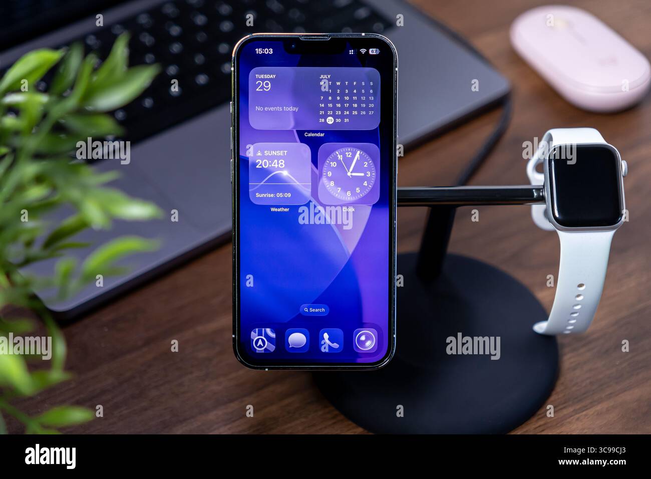 Poznan, Polonia - 29 luglio 2025: ios 26 mostra i widget dinamici sullo schermo in vetro liquido Apple iPhone, caricandoli con Apple Watch sulla scrivania moderna Foto Stock