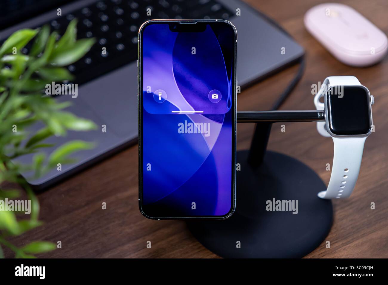 Poznan, Polonia - 29 luglio 2025: Smartphone Liquid Glass con ios 26, ricarica su piedistallo con smartwatch, per ottimizzare i moderni ambienti di lavoro connessi Foto Stock