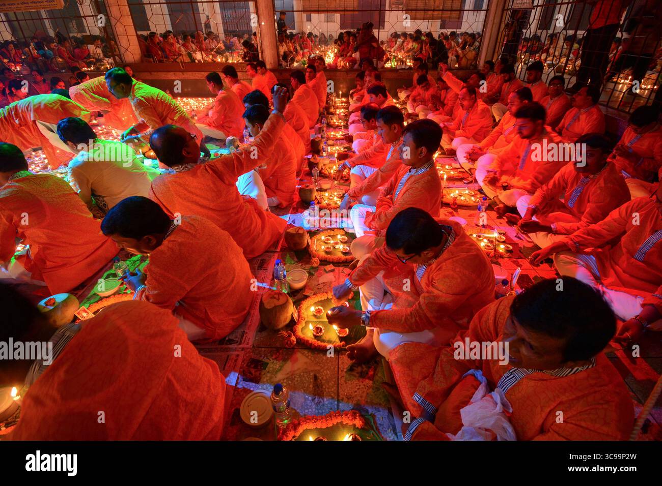 Dacca, Bangladesh - 13 novembre 2018: Veduta di un raduno di devoti in vivaci vesti arancioni, i loro volti illuminati dal soffice bagliore di numerose candele in un tempio. Foto Stock
