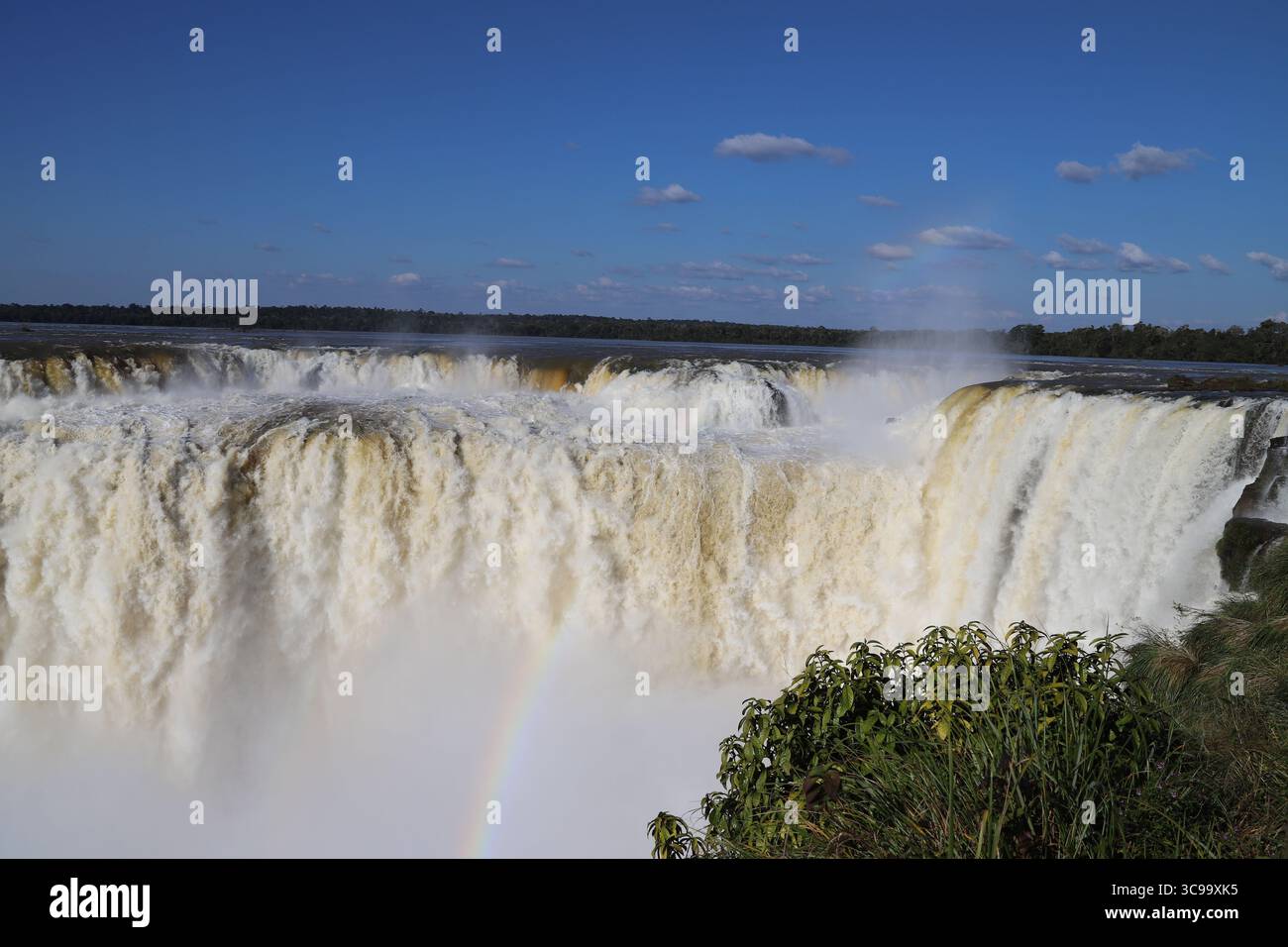Splendida vista delle cascate di Iguazú presso la Gola del Diavolo (Garganta del Diablo) con arcobaleno sul lato argentino, sotto un cielo blu brillante in una giornata di sole. Foto Stock