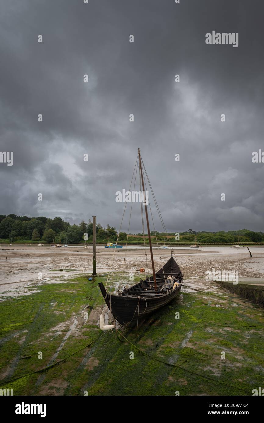Vecchia barca di legno con albero seduto sul fango sotto un cielo tempestoso. La banchina con la bassa marea sul fiume Deben nella storica città di Woodbridge nel Suffolk, Regno Unito Foto Stock