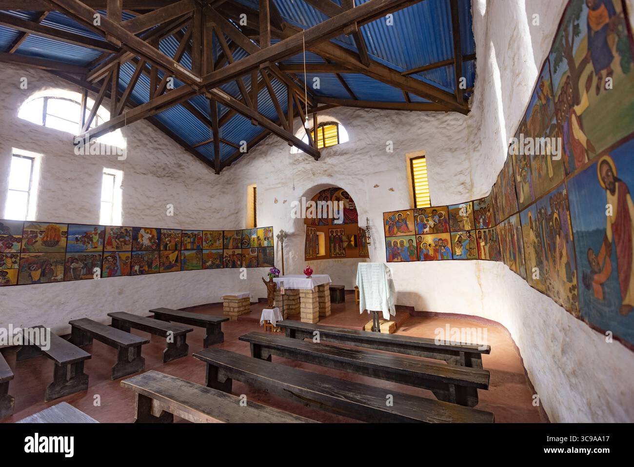 Kalacha, Kenya - 12 maggio 2022: Veduta dell'interno di una chiesa, dove la luce del sole scorre attraverso le finestre, illuminando i murales che fiancheggiano le pareti e le semplici panche di legno. Foto Stock