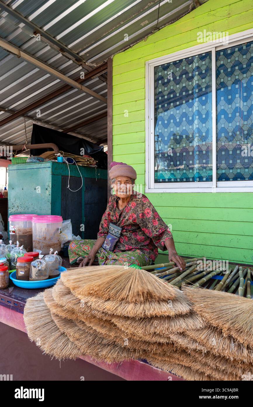 Provincia di Khon Kaen, Thailandia, 4 gennaio 2025: Un'anziana donna tailandese sorride mentre vende scope fatte a mano e altri condimenti locali da casa sua. Foto Stock