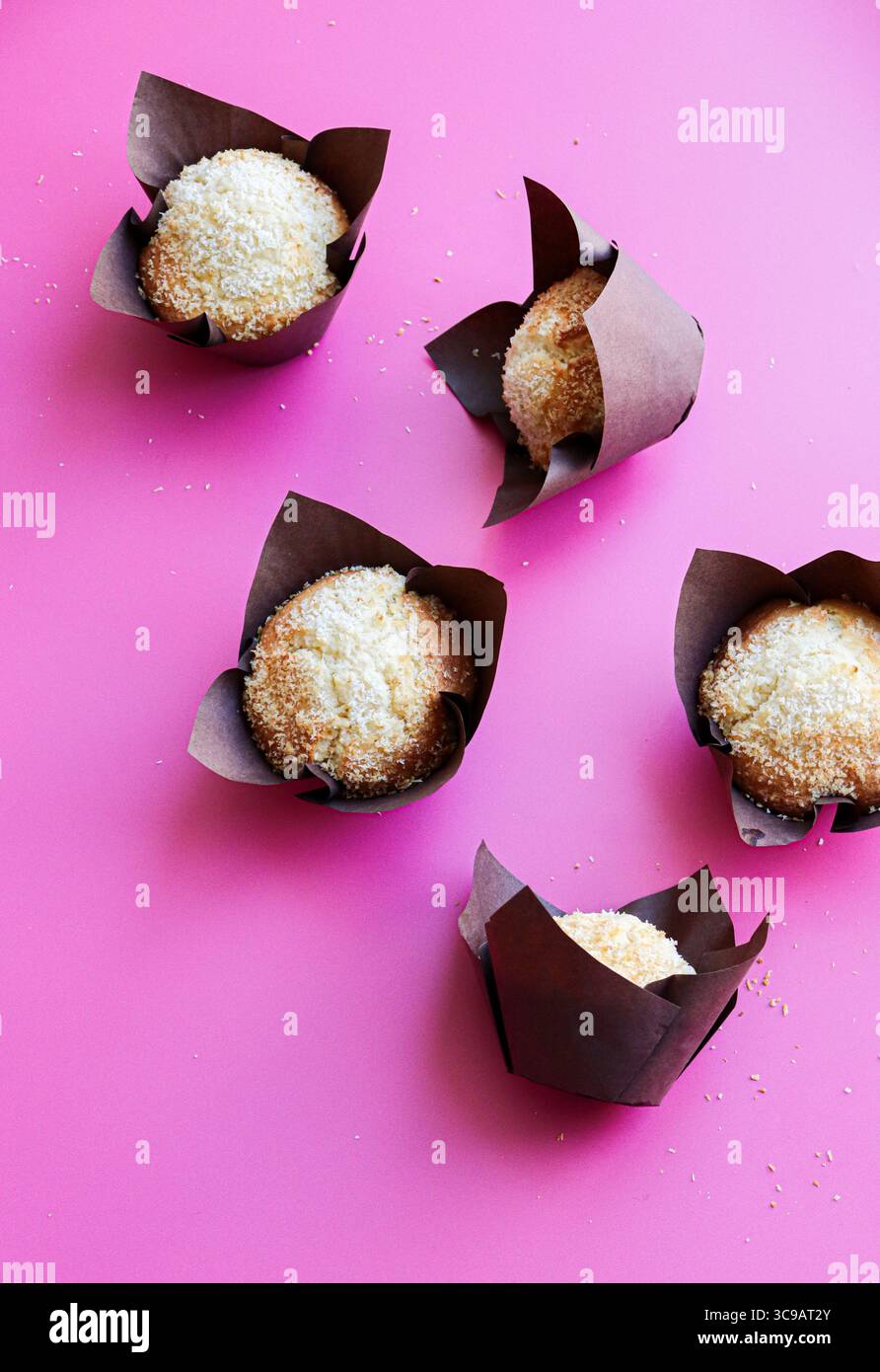 muffin marroni ricoperti di cocco in avvolgimenti marrone scuro in stile tulipano, disposti ad arte su un vivace sfondo rosa caldo. Foto Stock