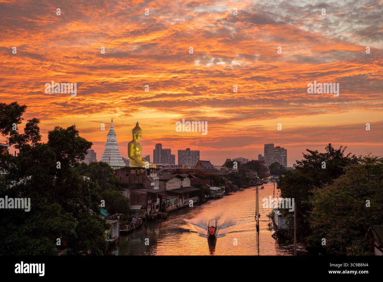 Una barca passava la statua del Grande Buddha (Phra Buddha Dhammakaya Thepmongkhon) nel tempio Wat Pak Nam Phasi Charoen situato vicino al fiume durante il tramonto. Foto Stock