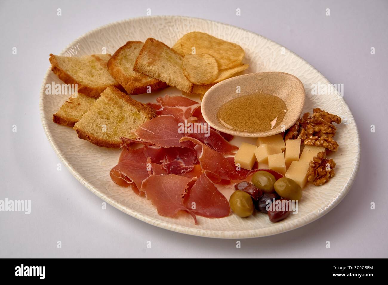 Un piatto ben organizzato con un assortimento di carni, formaggi e spuntini, perfetto per un incontro elegante o un'esperienza culinaria informale Foto Stock