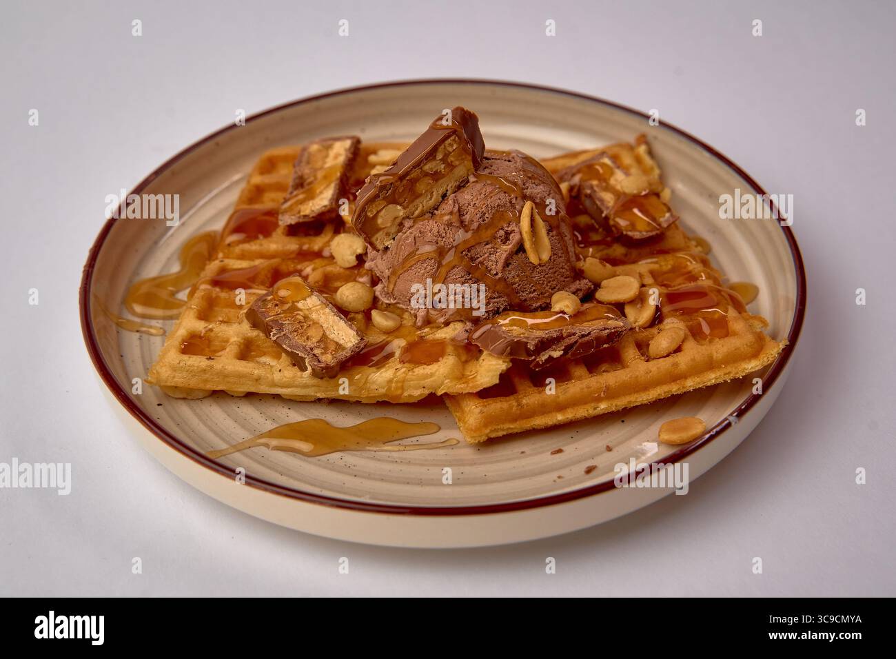 Deliziosi waffle conditi con un ricco gelato al cioccolato, conditi con sciroppo e guarniti con arachidi croccanti per un'esperienza di dessert appagante Foto Stock