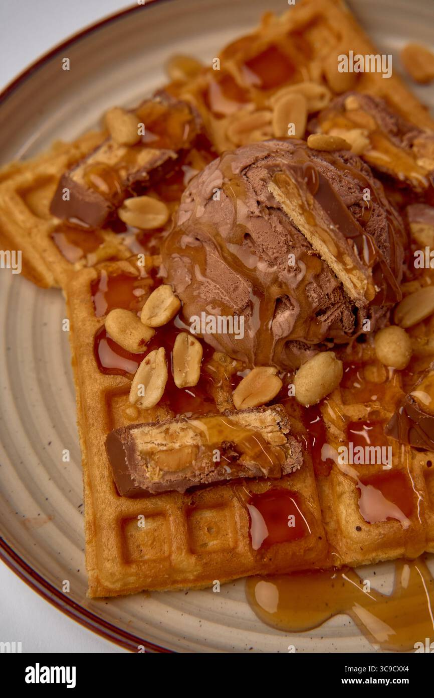 Waffle Delight con gelato al cioccolato, sciroppo e ricoperto di arachidi croccanti e barrette di cioccolato per una delizia irresistibile Foto Stock