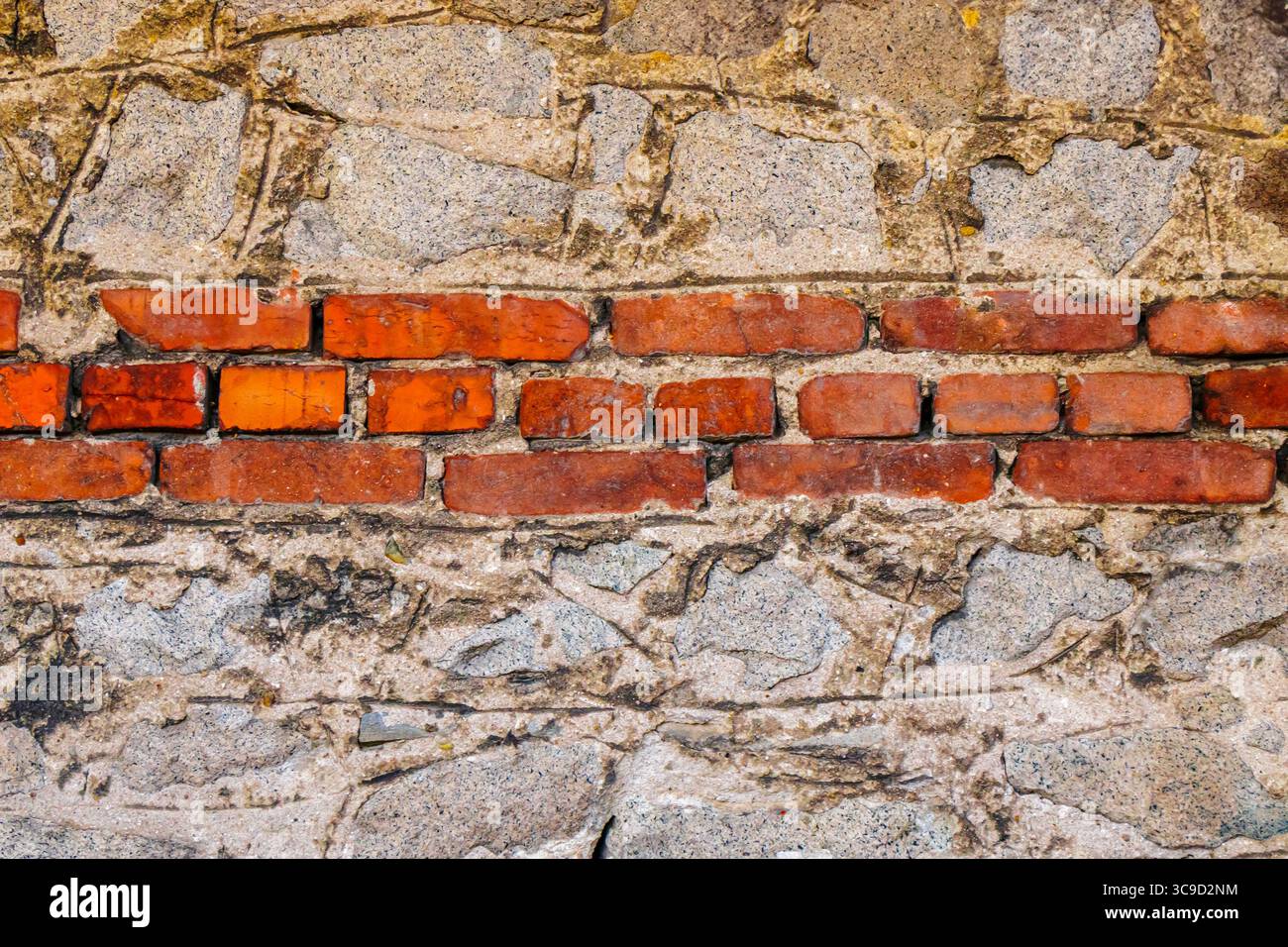 Vista dettagliata di un vecchio muro che combina pietra ruvida e mattoni rossi, mostrando l'artigianato e il passare del tempo nei materiali architettonici. Foto Stock