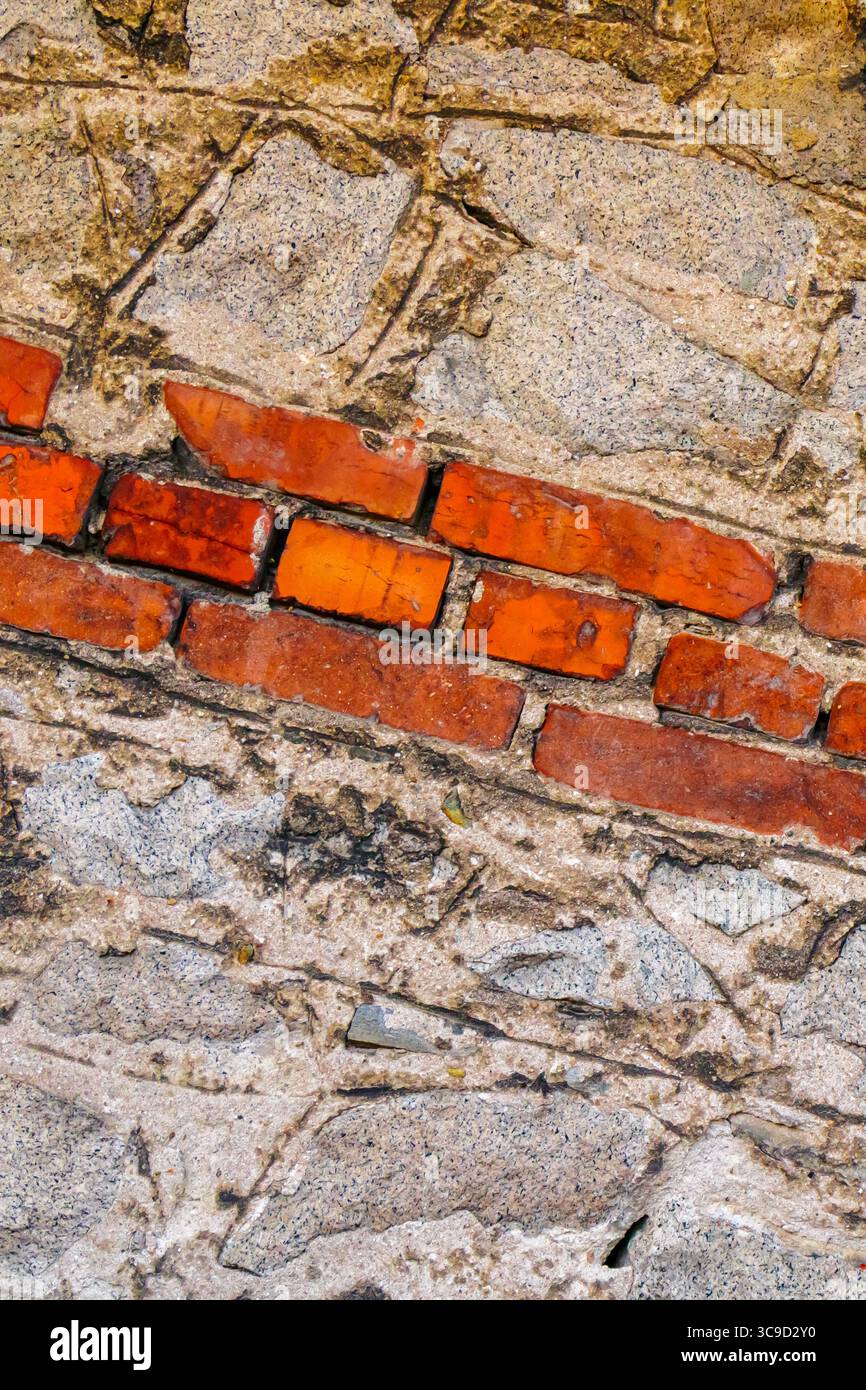 Un'immagine ravvicinata che mostra una linea diagonale di mattoni rossi incastonati in muratura grossa, evidenziando il contrasto tra materiali e età. Foto Stock