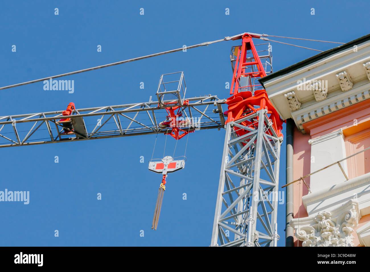 Un contrasto sorprendente tra un braccio rosso della gru e una facciata storica dell'edificio con dettagli classici ornati, catturati sotto la luce del giorno. Foto Stock