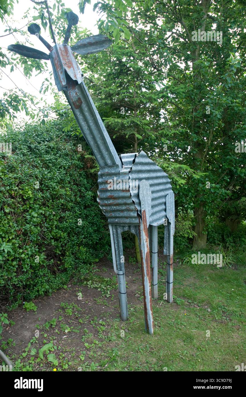 Una scultura creativa di giraffa in metallo si erge in alto nel verde, mostrando un'interpretazione artistica della fauna selvatica in un ambiente tranquillo all'aperto. Foto Stock