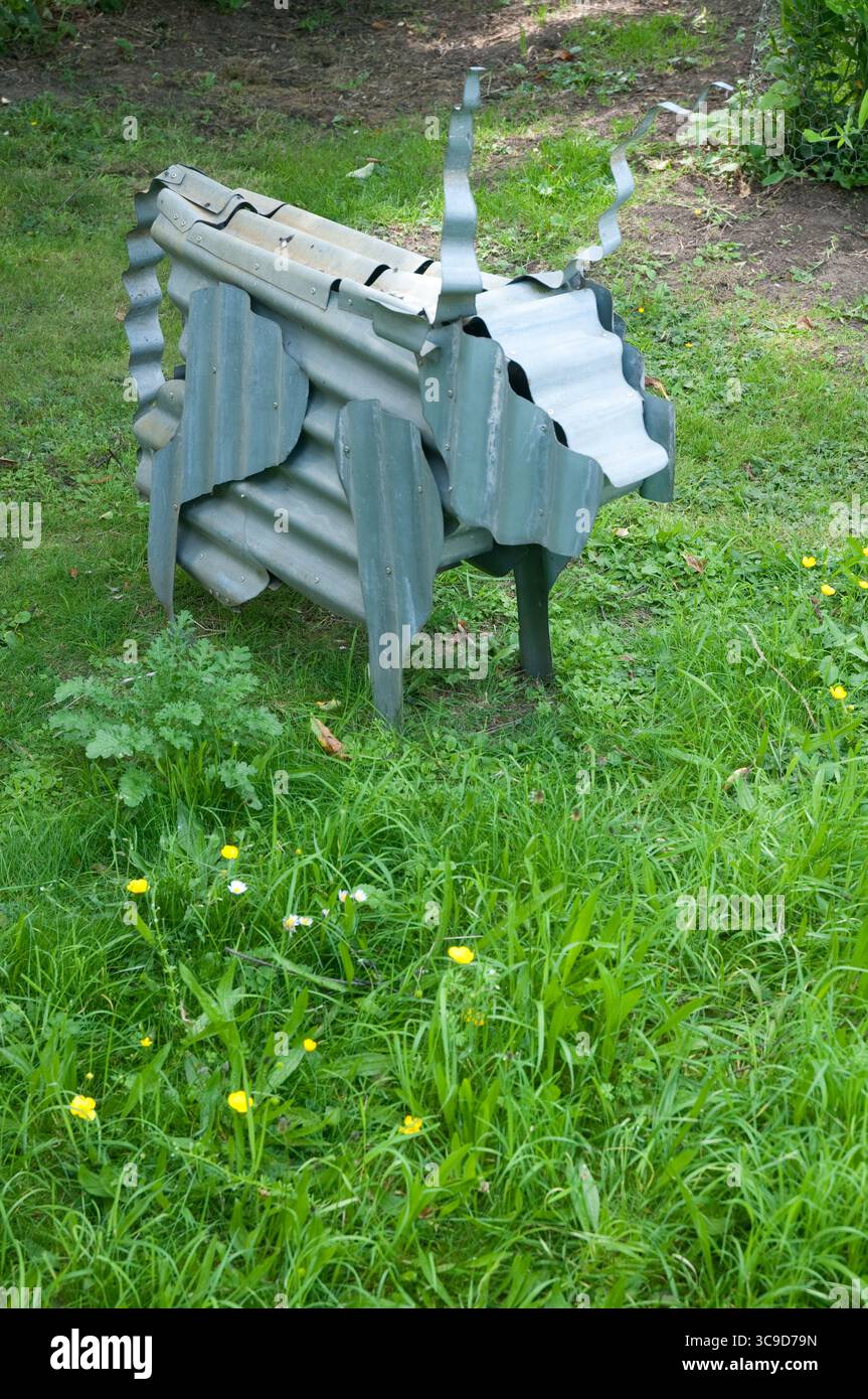 Una scultura in metallo realizzata in modo creativo, simile a un animale corneo, si trova tra i fiori selvatici in un paesaggio soleggiato del parco. Foto Stock