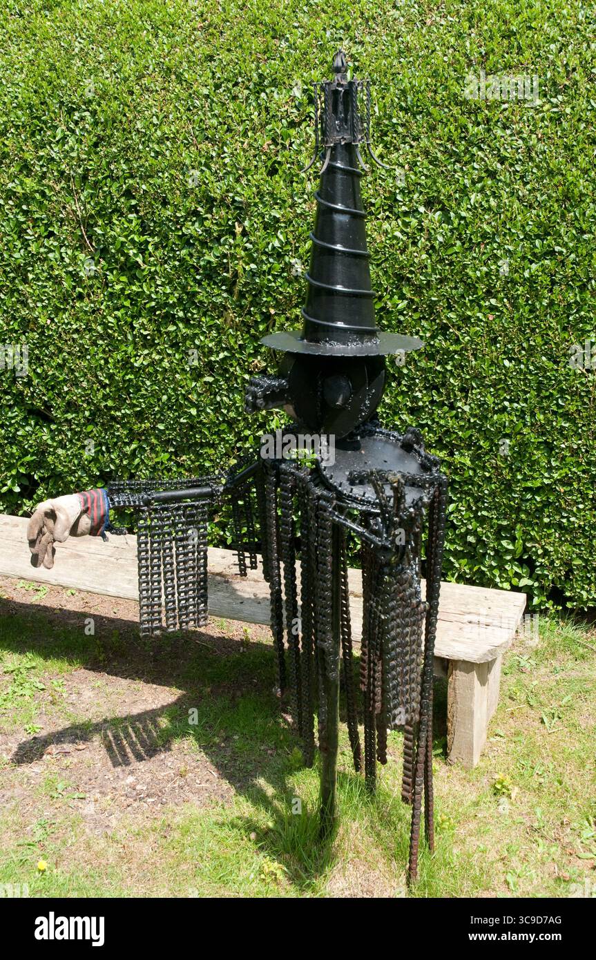 Una scultura unica realizzata con catene ed elementi metallici si erge in modo prominente in un lussureggiante giardino, che mostra dettagli intricati sotto la luce del sole. Foto Stock