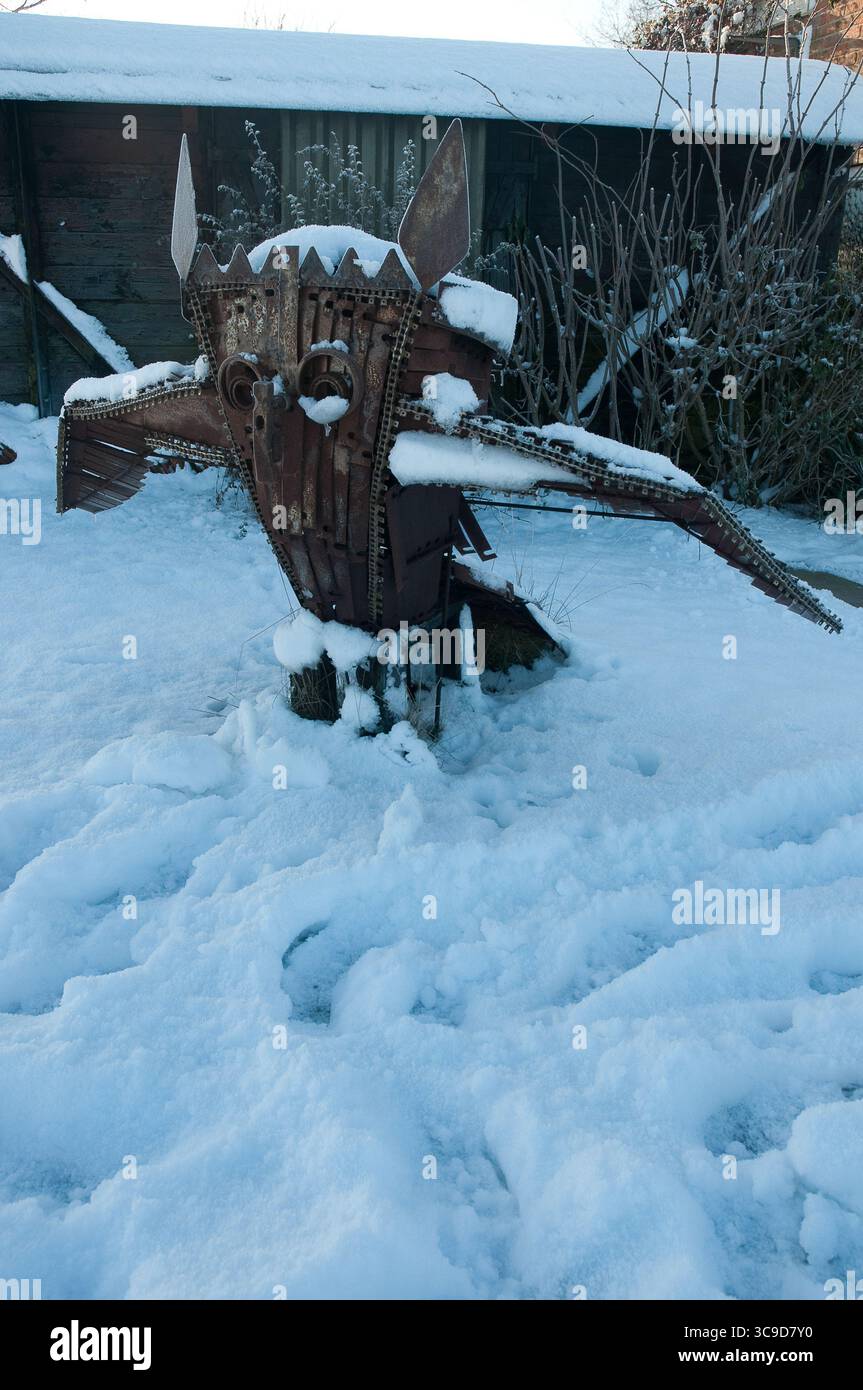 Scultura fatta di parti metalliche raffigura una figura animale, parzialmente sepolta nella neve in un ambiente freddo all'aperto circondato da arbusti. Foto Stock