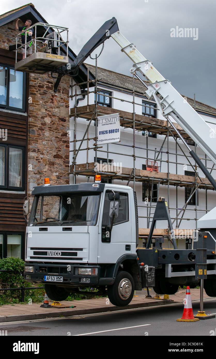 Un operaio edile su una piattaforma di gru che lavora all'esterno di un edificio a più piani circondato da impalcature Foto Stock Un operaio edile su una piattaforma di gru che lavora all'esterno di un edificio a più piani circondato da impalcature Foto Stock