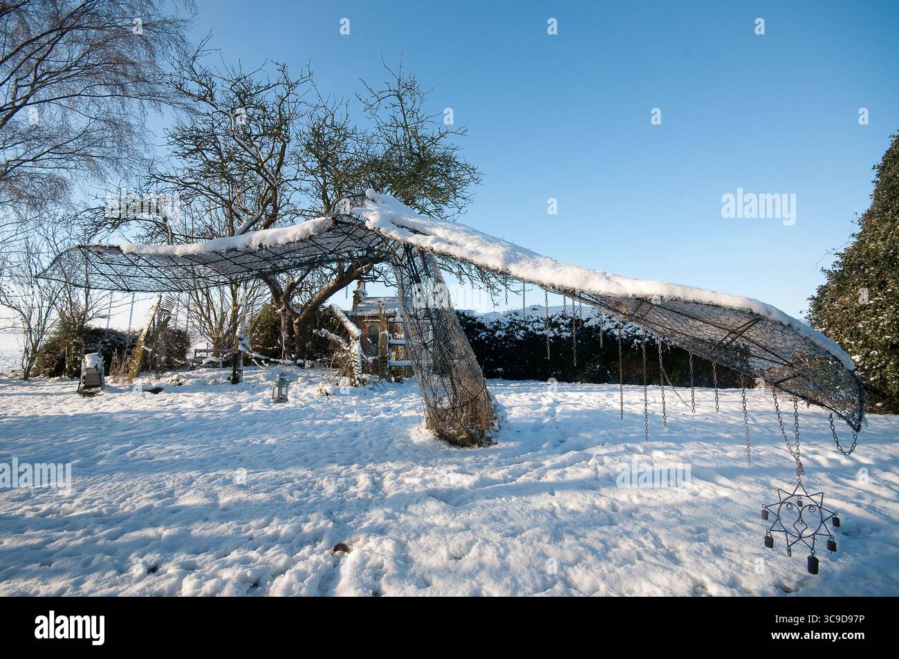 Un giardino unico ricoperto di neve si erge su un cielo blu luminoso, circondato da un tranquillo paesaggio invernale. Foto Stock