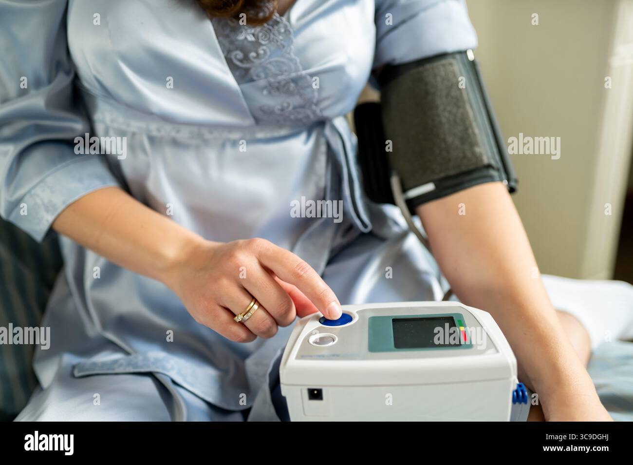 Donna che preme il pulsante sul monitor digitale della pressione sanguigna, inizia il controllo dello stato di salute, auto-monitoraggio e concetto di assistenza sanitaria domiciliare Foto Stock