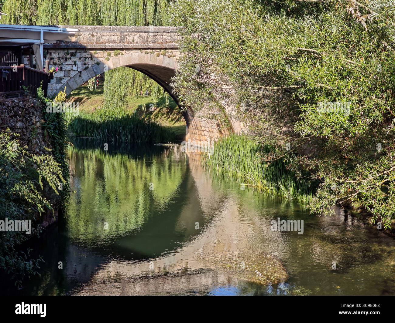 Il ponte di pietra di Ucero attraversa il fiume circondato da una vegetazione lussureggiante, che si riflette splendidamente nelle calme acque del nord della Spagna. Foto Stock