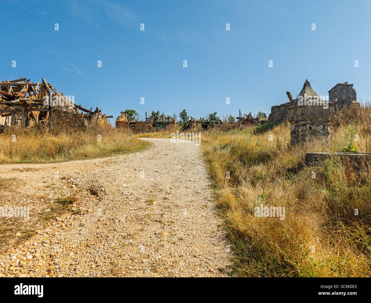 La silenziosa luce estiva illumina le case di pietra dimenticate lungo un sentiero polveroso a Cubillos, Soria, evocando ricordi di vite vissute una volta. Foto Stock