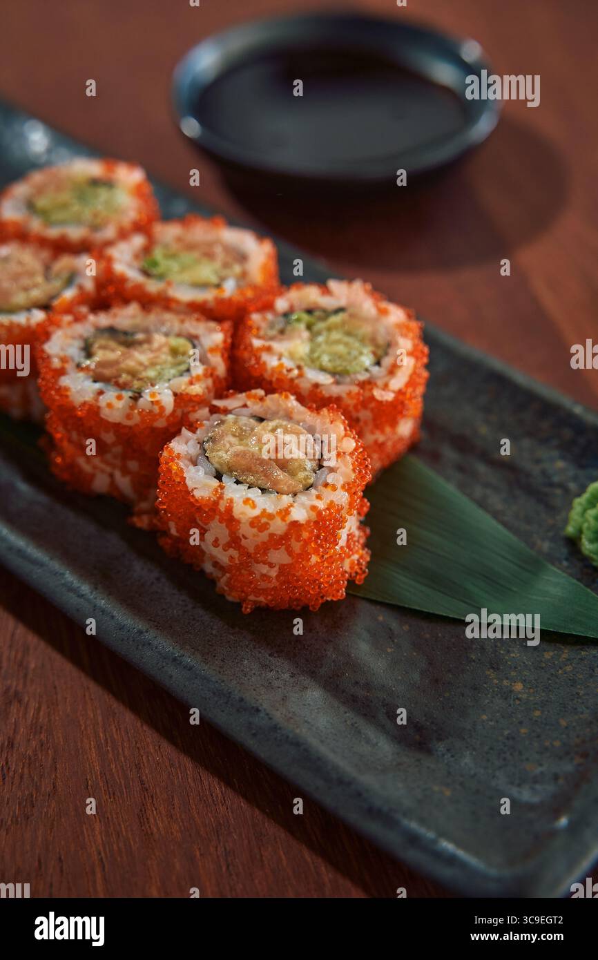 Delizioso primo piano di sushi Rolls condito con vivaci uova di pesce d'arancia e accompagnato da salsa di soia e Wasabi su un piatto elegante Foto Stock
