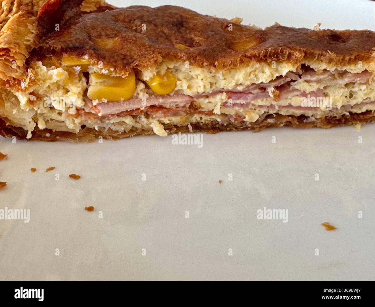 Vista laterale di una quiche fatta in casa con strati di prosciutto, formaggio, mais e una crosta di pasta marrone dorata, fotografata su sfondo bianco. Foto Stock