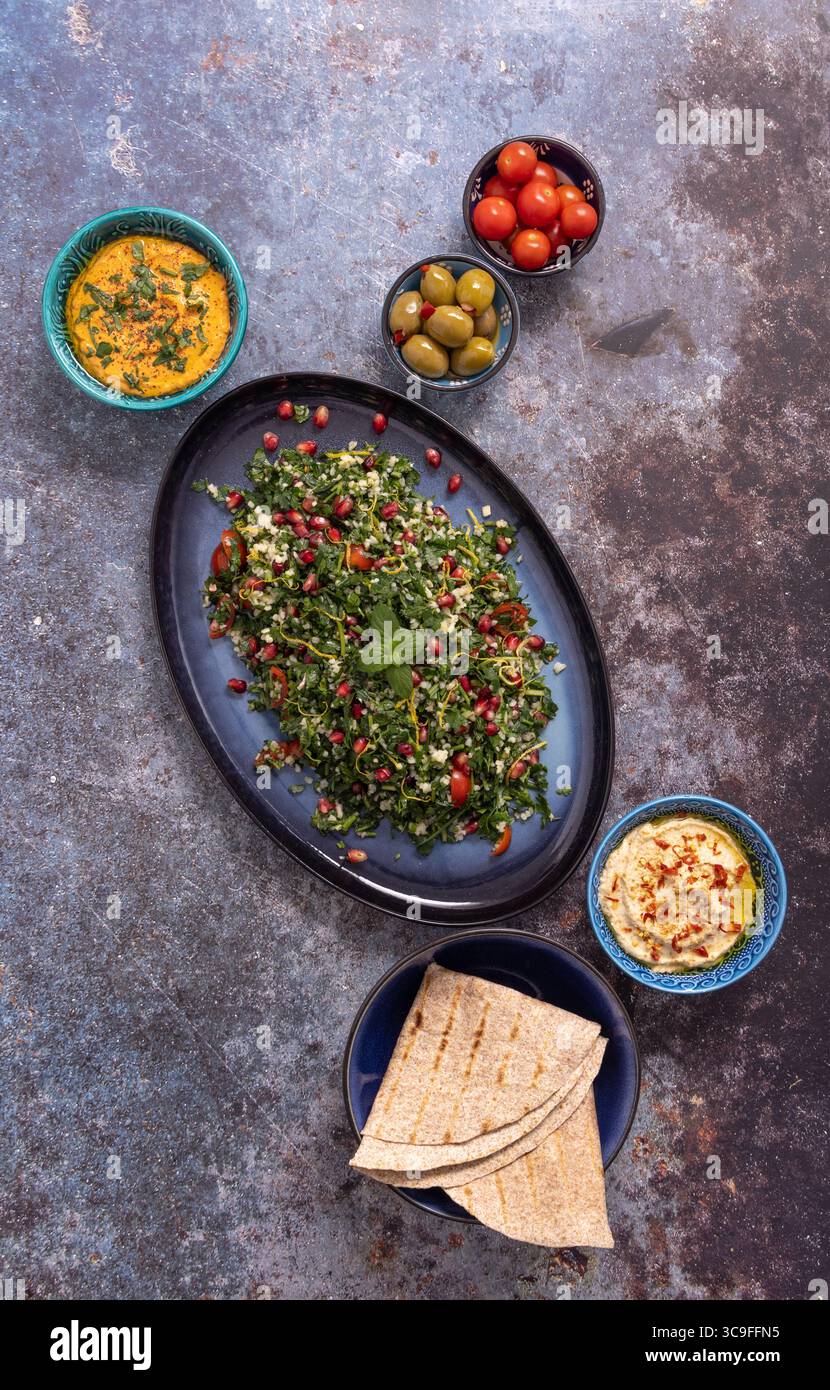 Insalata di tabbouleh con hummus, salse, olive e focaccia. Un mezze vibrante e a misura d'istinto, disegnato su una superficie rustica. A base vegetale e fresca. Foto Stock