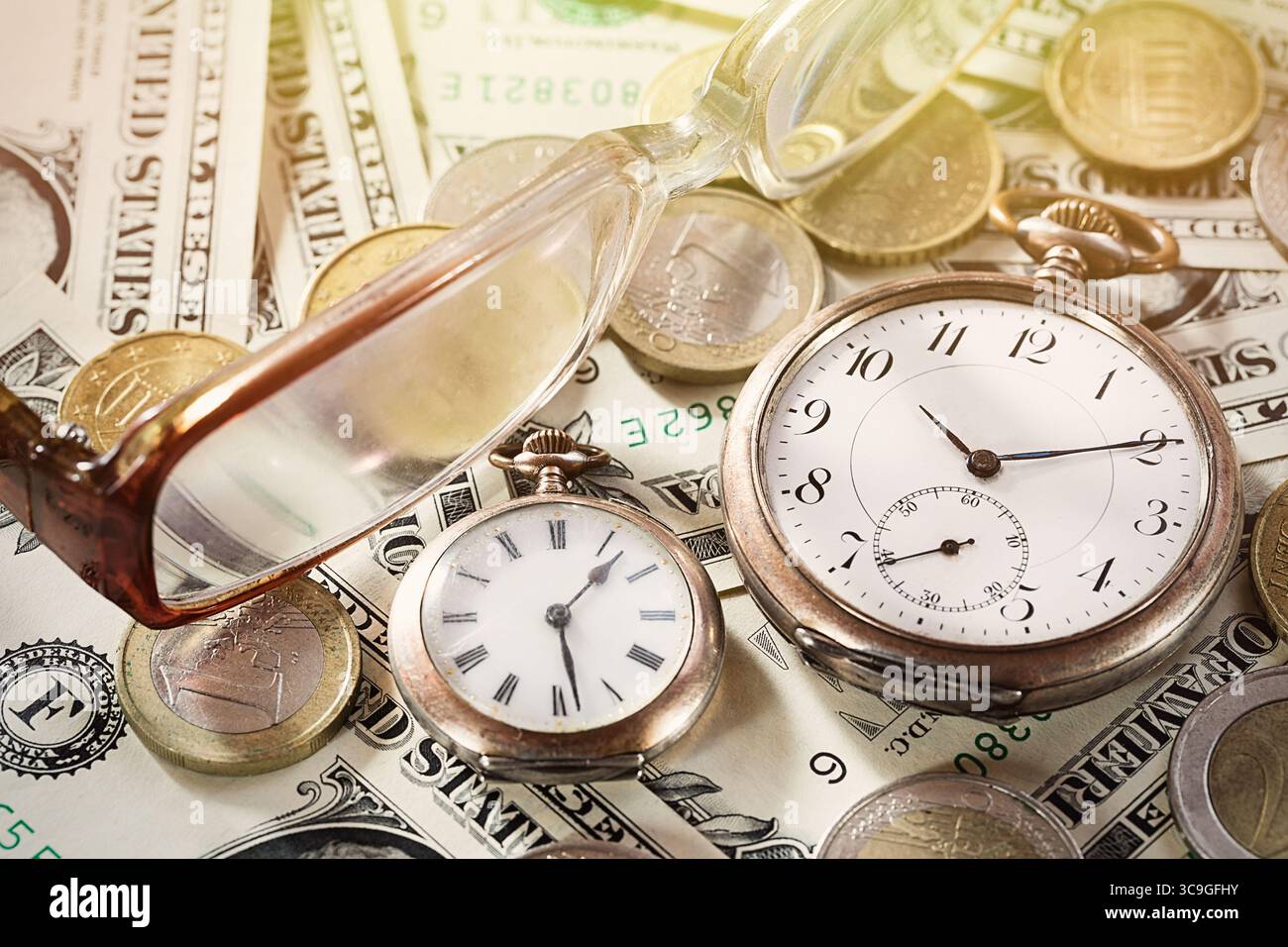 Il tempo è un concetto di finanza monetaria con vecchi orologi vintage, banconote da un dollaro, monete in euro e occhiali. Foto Stock