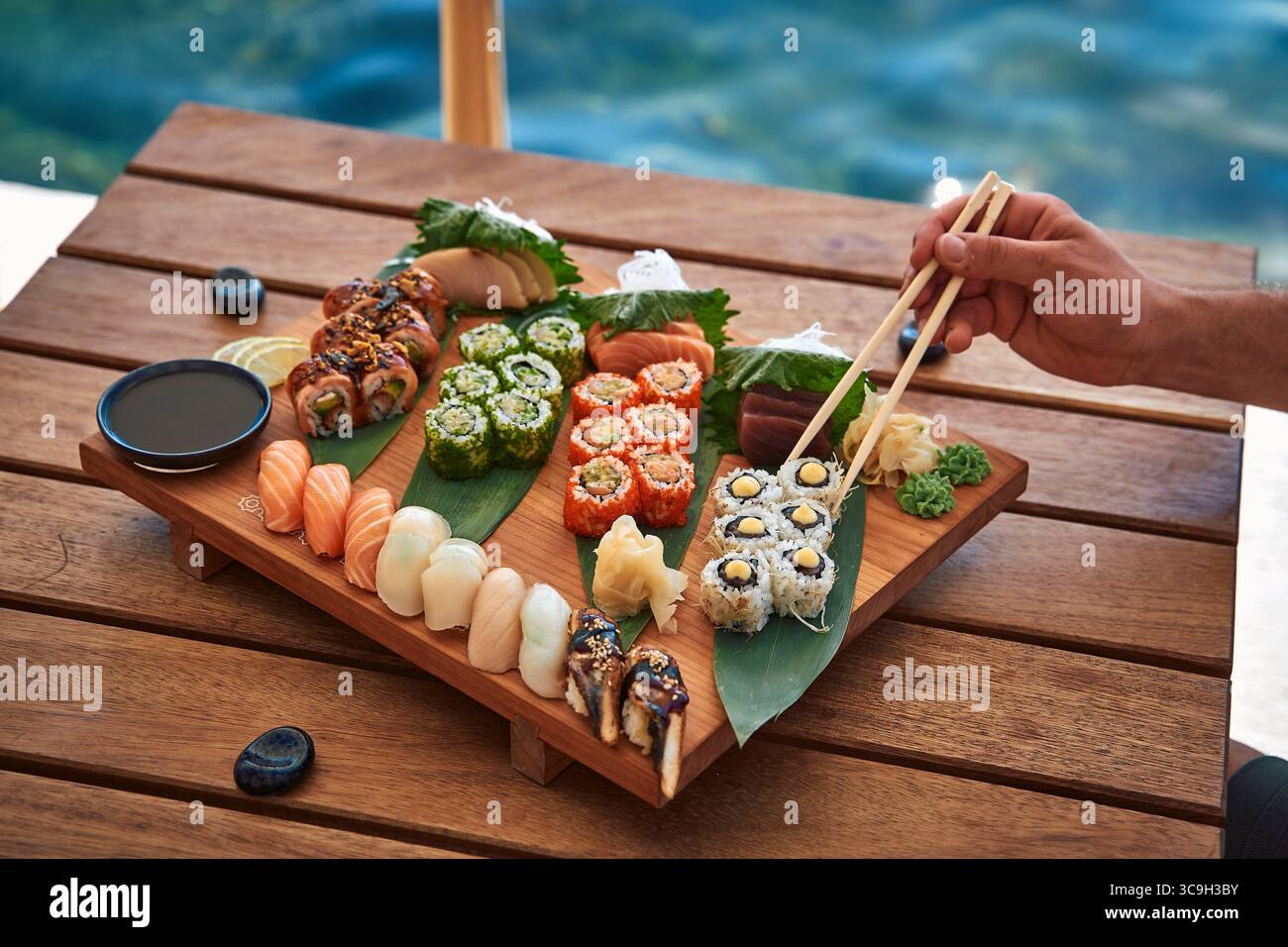 Uno squisito piatto di sushi presentato ad arte su una tavola di legno, caratterizzato da diverse varietà, tra cui Maki, Sashimi e Rolls colorati con Dippi Foto Stock