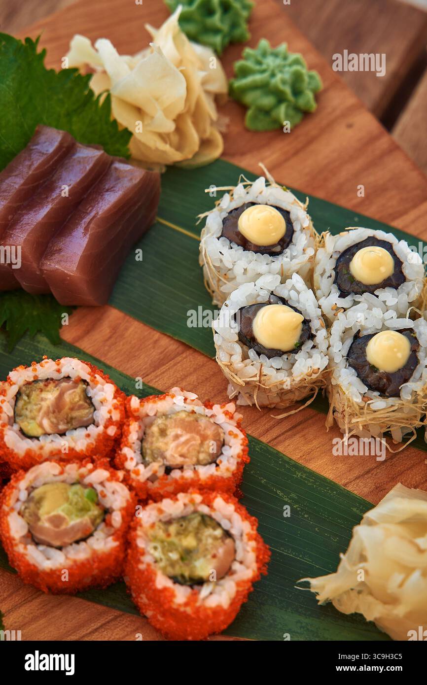 Un colorato piatto di sushi che mostra vari tipi di panini di sushi, pesce fresco, Wasabi e zenzero martellato su una tavola da servizio in legno Foto Stock
