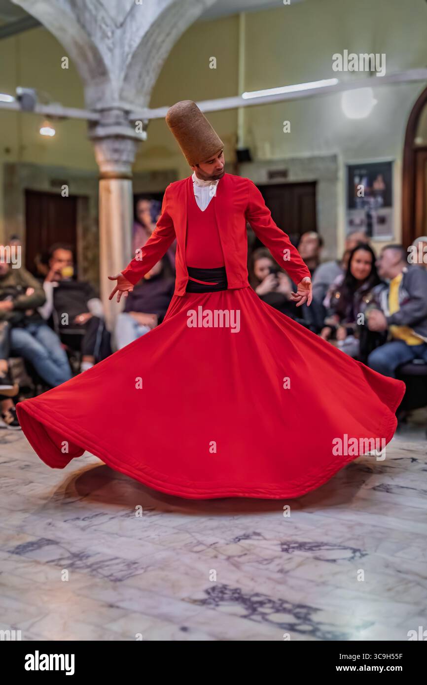 Istanbul, Turchia - 11 novembre 2023: Un derviscio vorticoso in una veste rossa e un cappello alto esegue una tradizionale cerimonia Sema, che scorre largo mentre gira Foto Stock