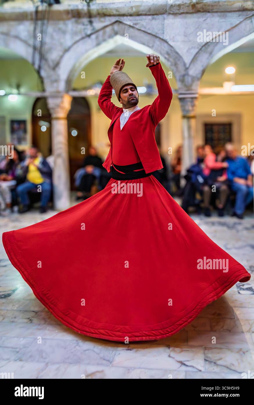 Istanbul, Turchia - 11 novembre 2023: Un derviscio vorticoso in una veste rossa e un cappello alto esegue una tradizionale cerimonia Sema, che scorre largo mentre gira Foto Stock