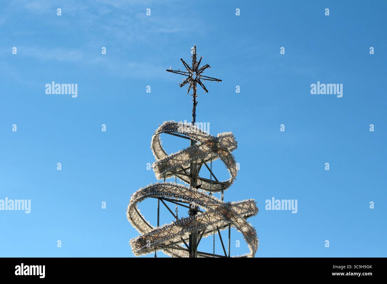 Una scultura metallica presenta una ghirlanda bianca a spirale e un topper a stella, appoggiato in modo netto su un cielo blu vivace, che evoca una vacanza contemporanea Foto Stock