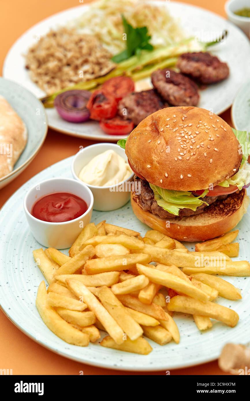Deliziosa combinazione di hamburger classico con verdure fresche, patatine fritte e salse piccanti in un'appetitosa presentazione culinaria Foto Stock