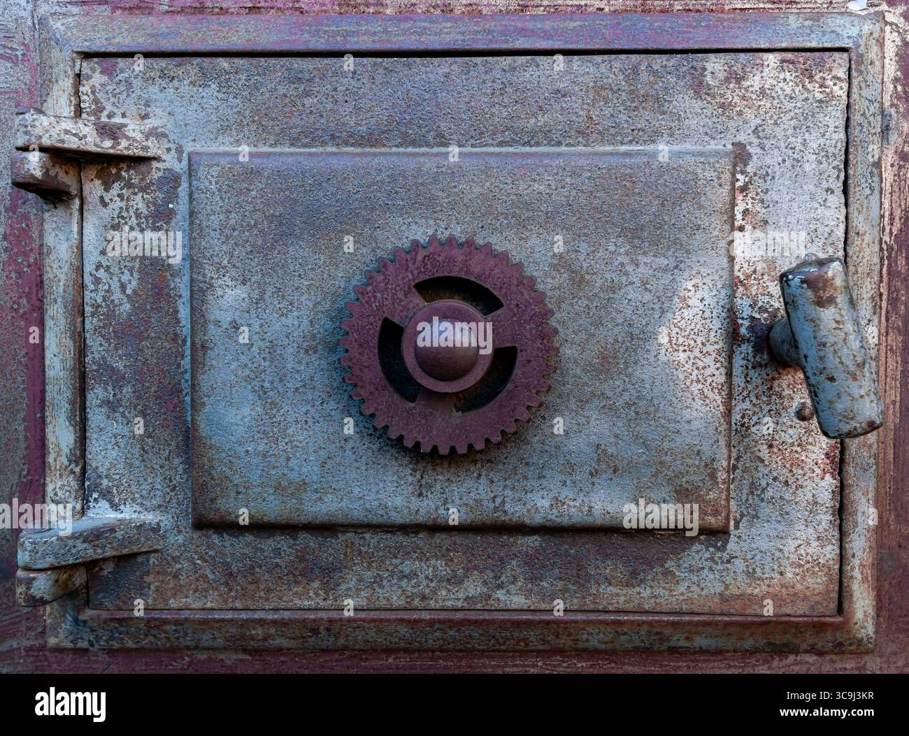 Porta della stufa in ghisa vintage con apertura a ingranaggi sul vecchio sito ferroviario, texture industriale e primo piano su patina. Foto Stock