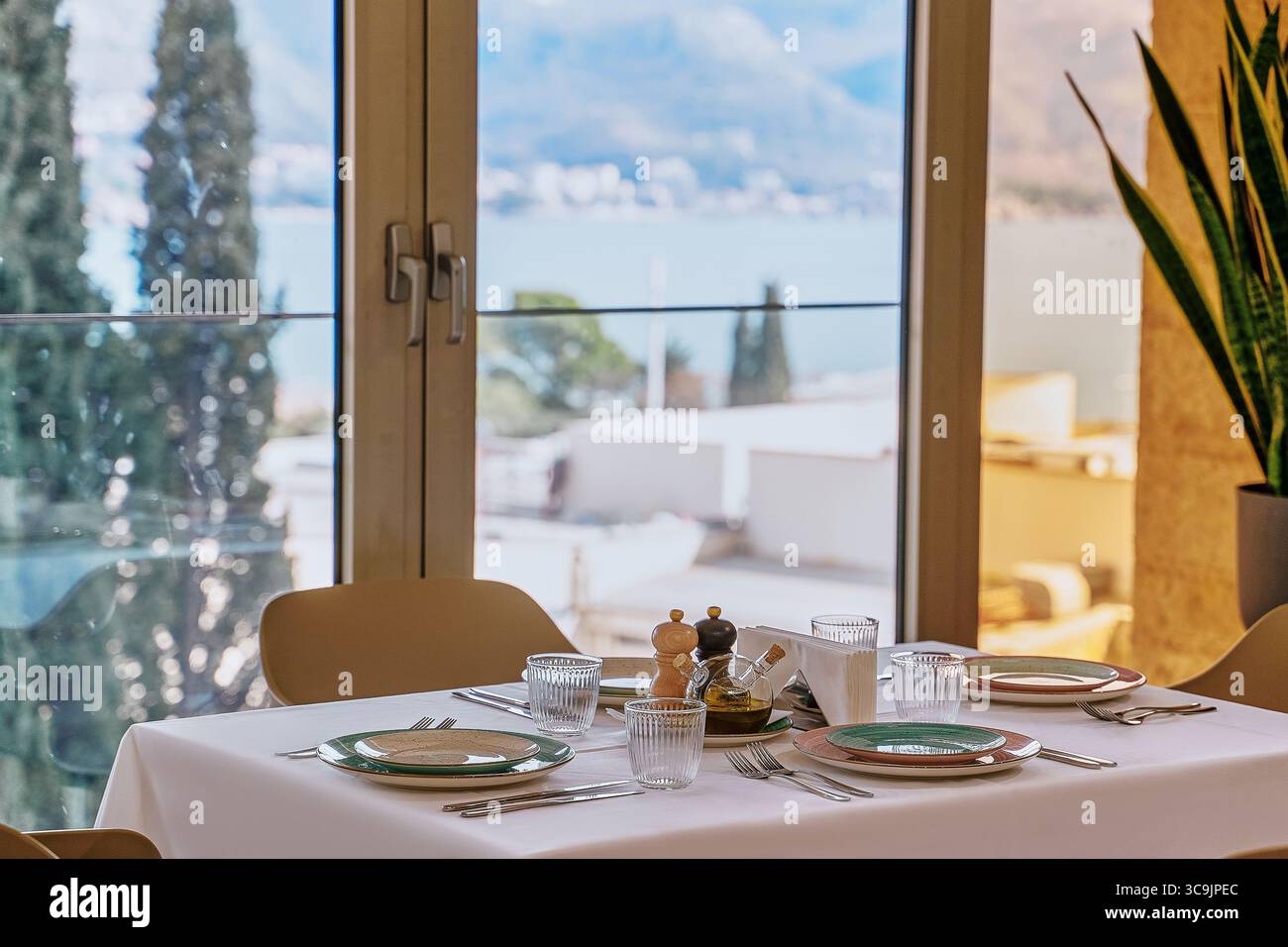 Elegante sala da pranzo con vista panoramica sull'acqua e sulle montagne, con stoviglie e luci soffuse per un'atmosfera accogliente Foto Stock