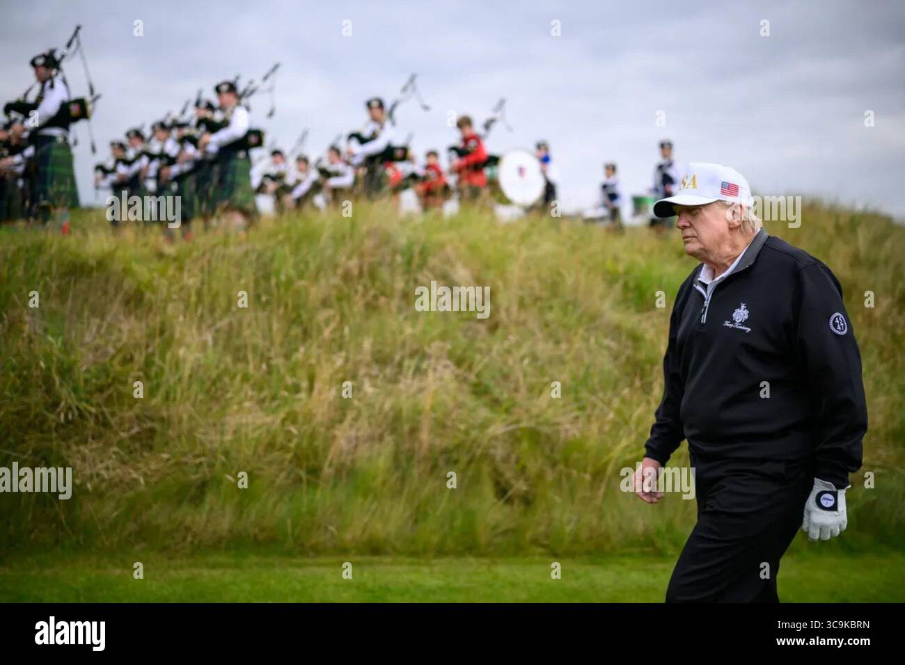 Il presidente Donald J. Trump cammina sul campo da golf di Trump Turnberry mentre una banda scozzese di cornamuse si esibisce durante la sua visita in Scozia. Il momento ha mescolato tradizione e affari personali durante il suo viaggio diplomatico di cinque giorni. Scozia. Luglio 2025. Per gentile concessione della Casa Bianca. Foto Stock