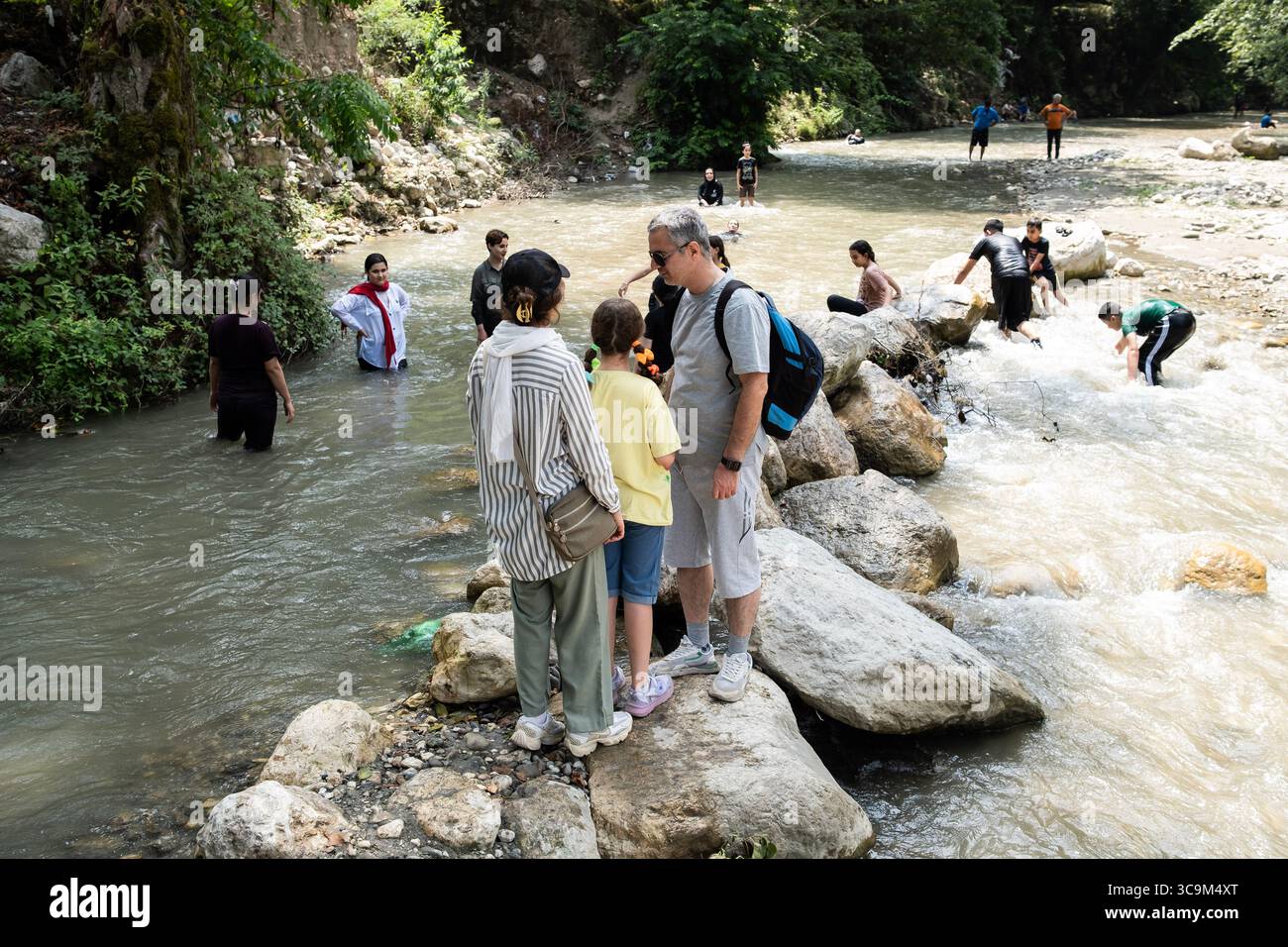 Chalus, Iran. 1 agosto 2025. Una famiglia sta su una roccia nel fiume, mentre diverse persone giocano in acqua. L’ondata di caldo senza precedenti in Iran ha portato a un consumo di elettricità diffuso, causando la chiusura degli uffici governativi. In molte città del nord come Chalus, la gente si rivolge alle attività acquatiche lungo il fiume per sfuggire al caldo estremo.Chalus è una città situata nella provincia settentrionale di Mazandaran in Iran. (Foto di Alborz Irani/SOPA Images/Sipa USA) credito: SIPA USA/Alamy Live News Foto Stock