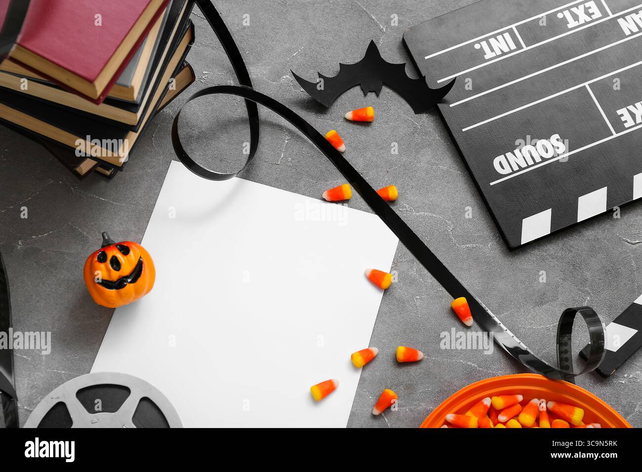 Clapperboard con bobina di pellicola, caramelle e carta bianca su sfondo grigio grunge. Festa di Halloween Foto Stock