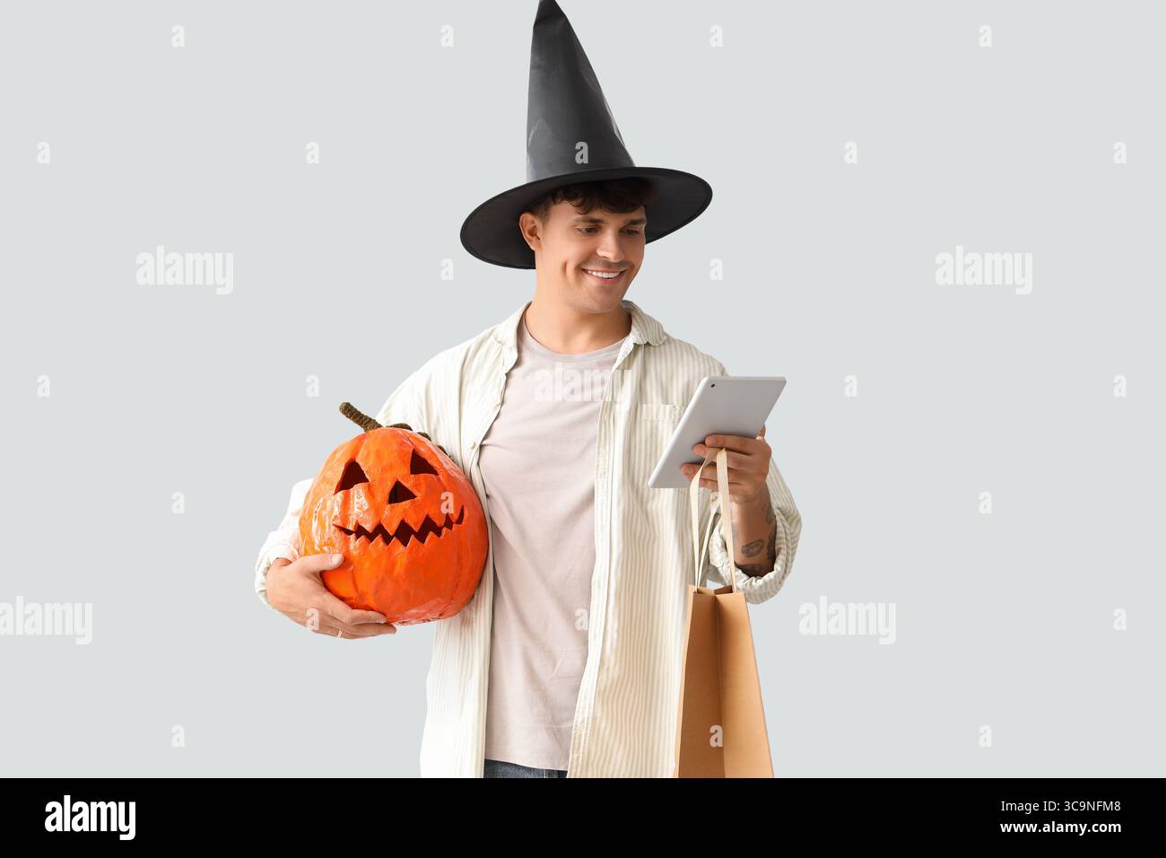 Giovane in cappello mago con zucca di Halloween e tablet computer che fa acquisti online su sfondo chiaro Foto Stock