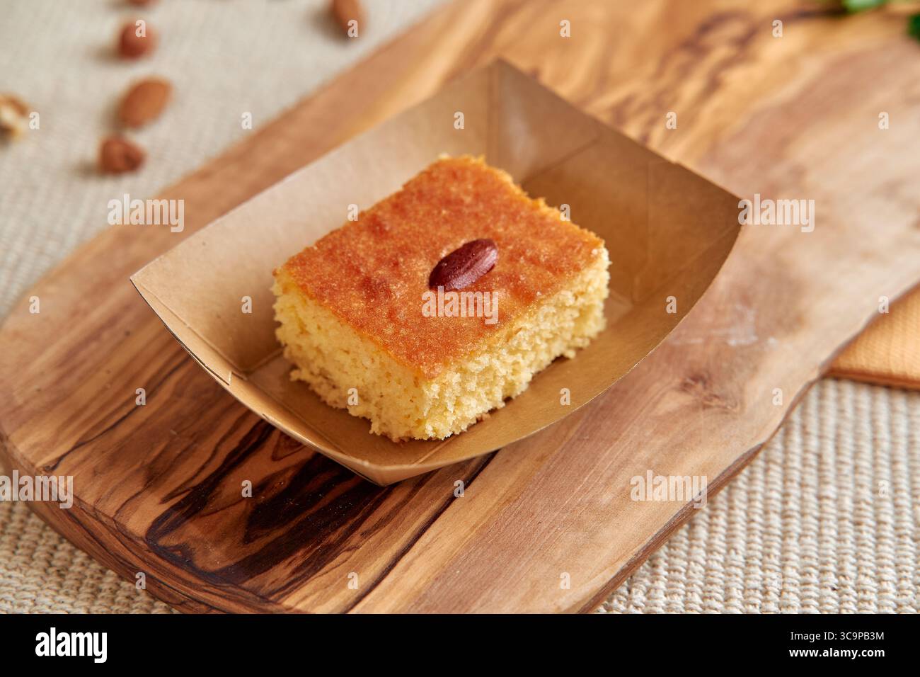 Deliziosa fetta di torta umida e saporita esposta su una tavola da servizio in legno rustico con contorno di mandorle per invitanti dessert Foto Stock