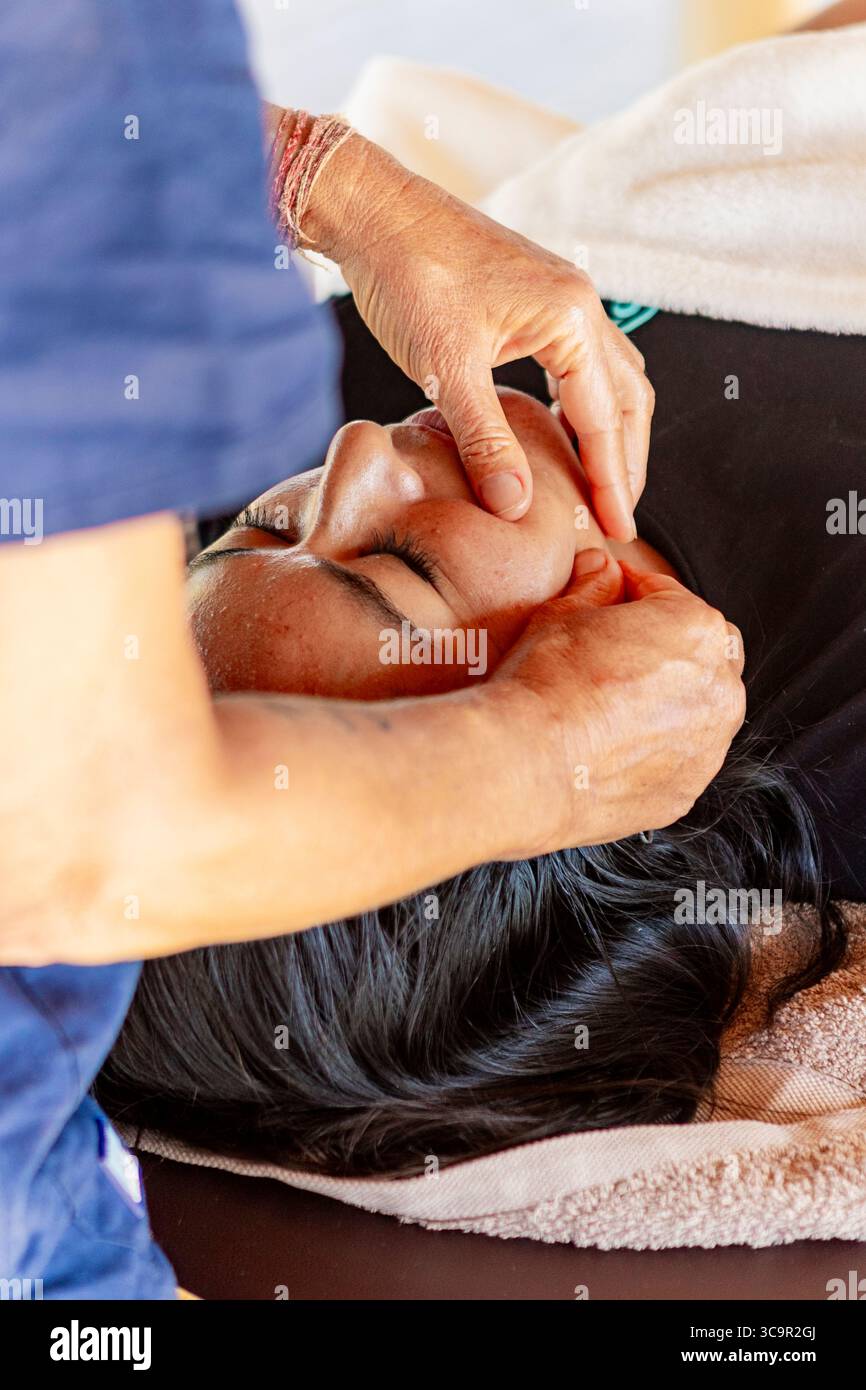 Primo piano delle mani di un massaggiatore che lavora dolcemente sul viso di un cliente durante una sessione di massaggio rilassante Foto Stock