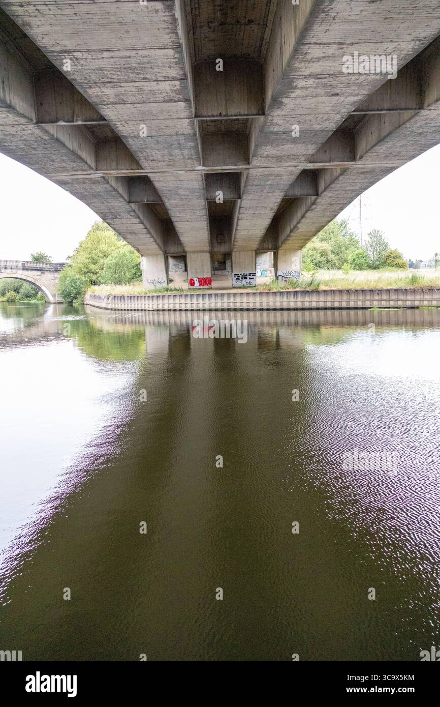 Struttura in cemento che si riflette nelle calme acque del fiume, vista da sotto in una giornata coperta Foto Stock
