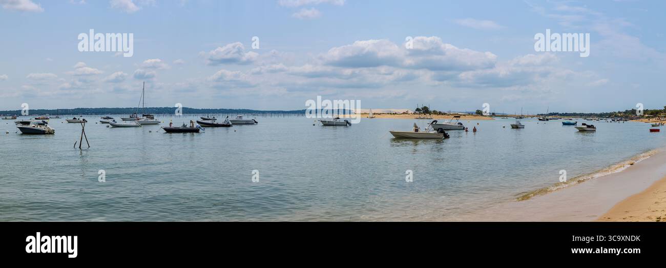 Cap Ferret, Francia - 3 luglio 2025: Panorama della baia di Arcachon dalla spiaggia di Mimbeau, artigianato in primo piano, Duna di Pilat sullo sfondo Foto Stock
