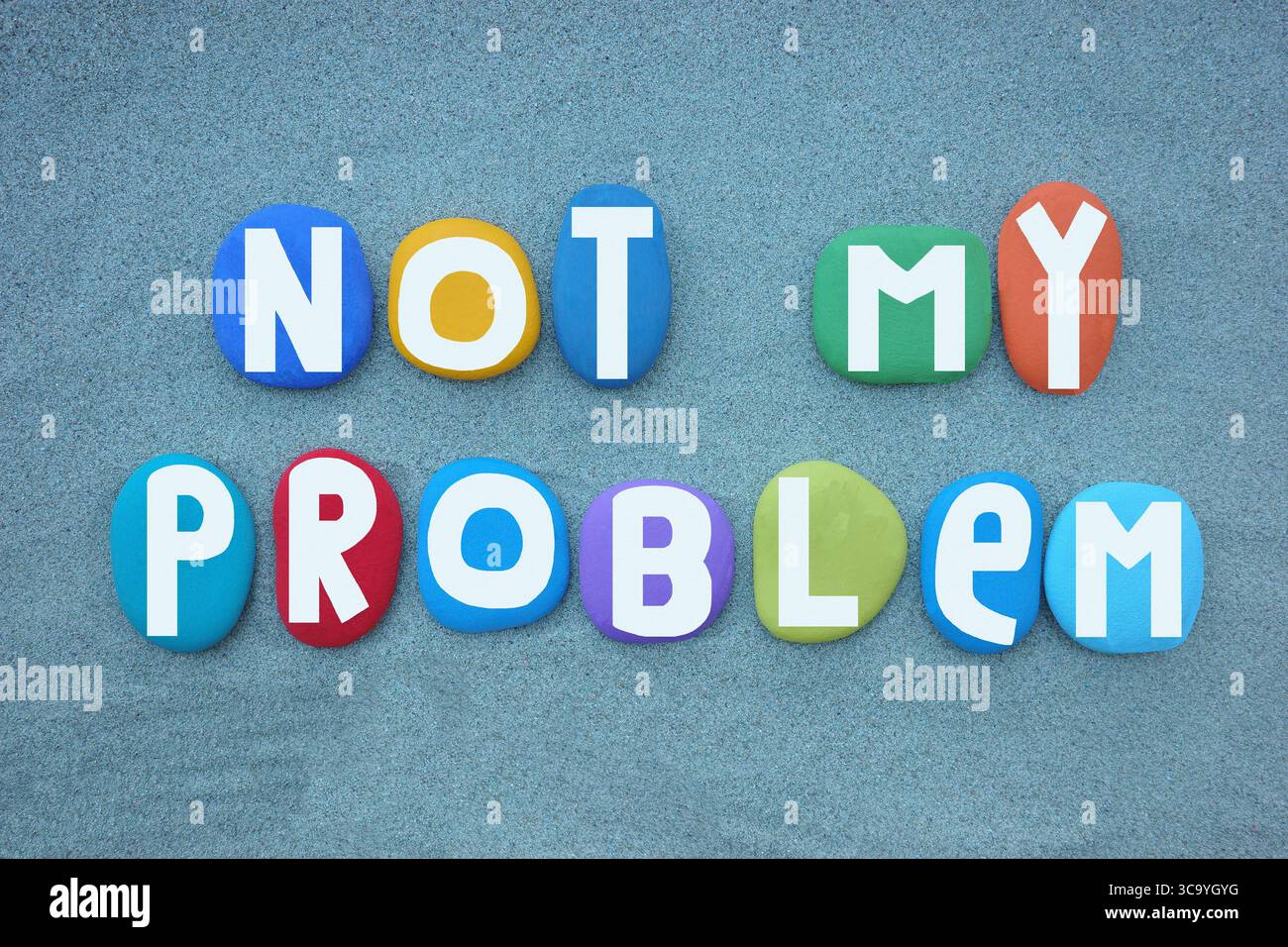 Non è un mio problema, slogan motivazionale composto da lettere di pietra dipinte a mano multicolore su sabbia verde Foto Stock